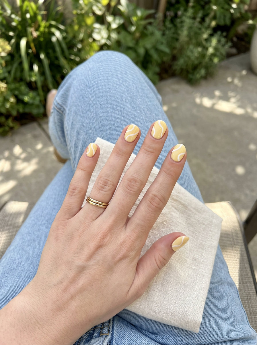 Short round summer nails 2026: Butter yellow with abstract white swirls for casual outings and picnics.